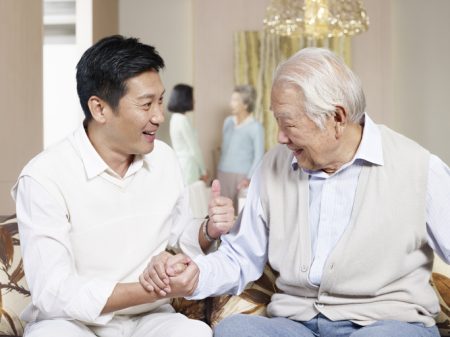 asian father and son chatting on couch.